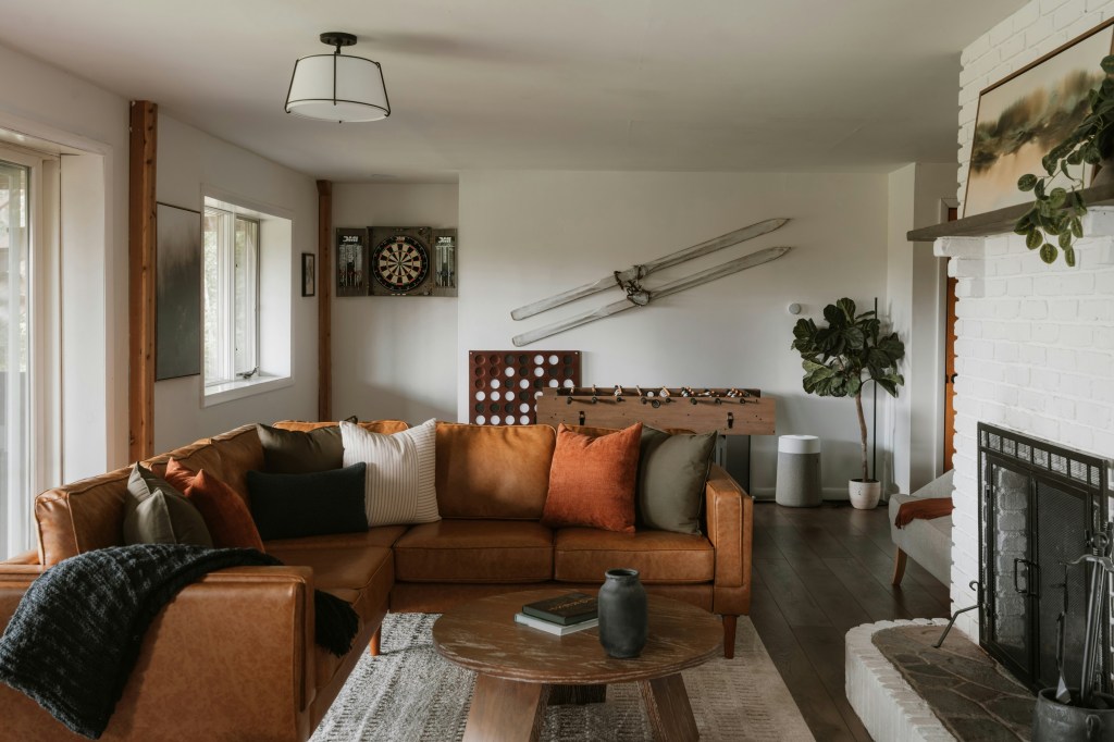 Cozy basement living room with a warm caramel coloured leather sofa, soft textiles, wood accents, neutral décor and separate areas for activates creating a grounded and inviting atmosphere.